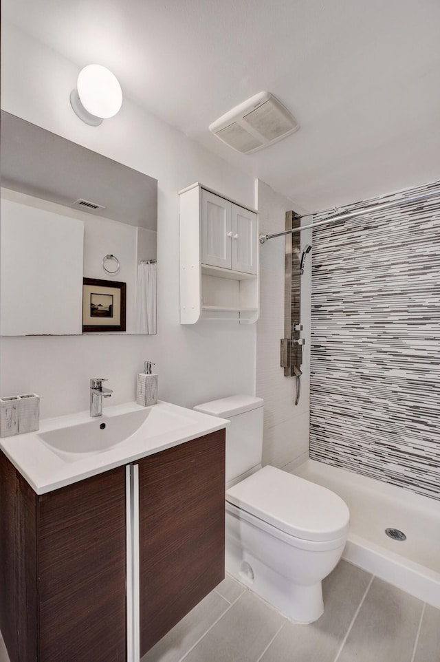 bathroom featuring toilet, vanity, tile patterned flooring, and tiled shower