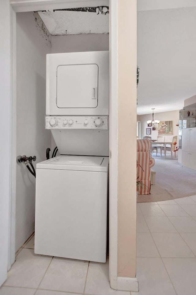 laundry area with a notable chandelier, stacked washing maching and dryer, and light tile patterned floors