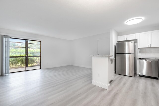 kitchen featuring appliances with stainless steel finishes, light wood-type flooring, light stone counters, decorative backsplash, and white cabinetry