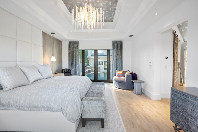 bedroom featuring a barn door, a raised ceiling, light wood-type flooring, crown molding, and an inviting chandelier