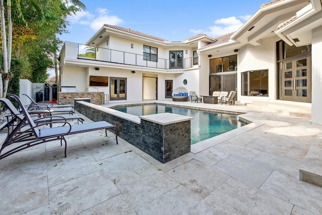 back of property with exterior bar, a balcony, a swimming pool with hot tub, and a patio