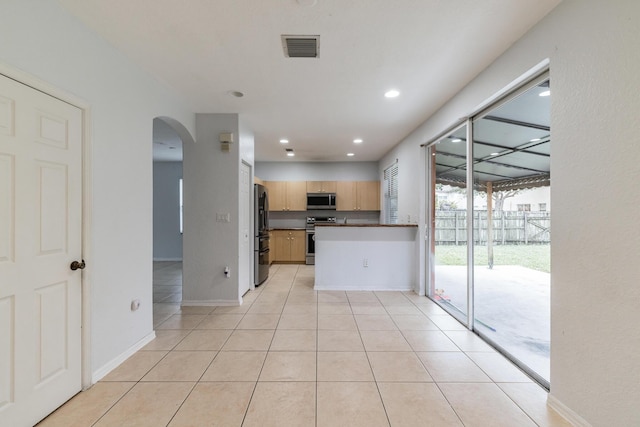 kitchen with kitchen peninsula, light brown cabinetry, appliances with stainless steel finishes, and light tile patterned floors