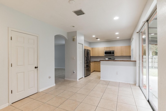 kitchen with appliances with stainless steel finishes, light tile patterned floors, kitchen peninsula, and light brown cabinets