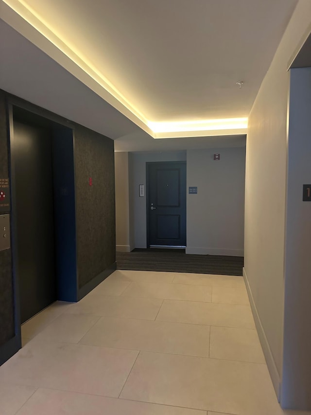 corridor with light tile patterned floors and a tray ceiling