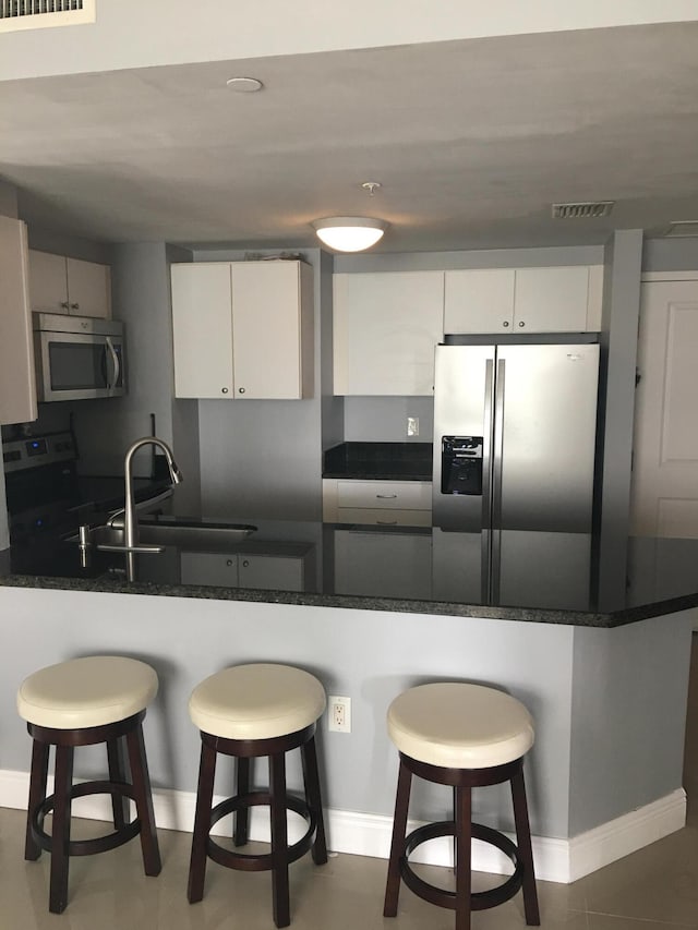 kitchen with white cabinetry, stainless steel appliances, a kitchen breakfast bar, and kitchen peninsula