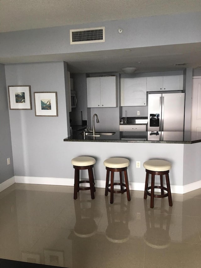 kitchen featuring stainless steel appliances, a breakfast bar, sink, white cabinetry, and kitchen peninsula