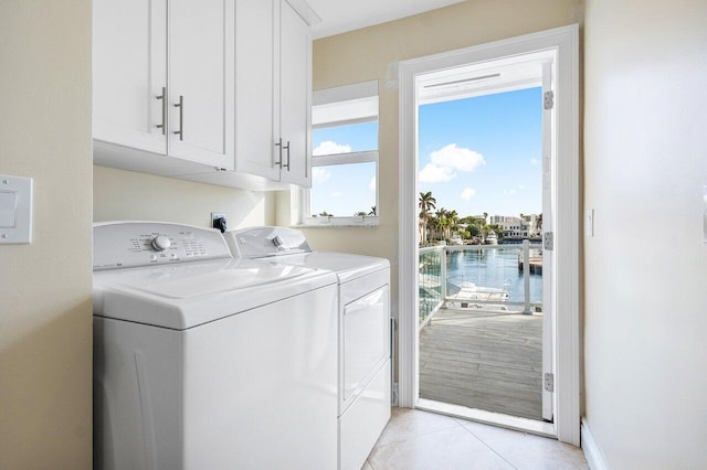 laundry room featuring cabinets, light tile patterned floors, a water view, and washing machine and clothes dryer