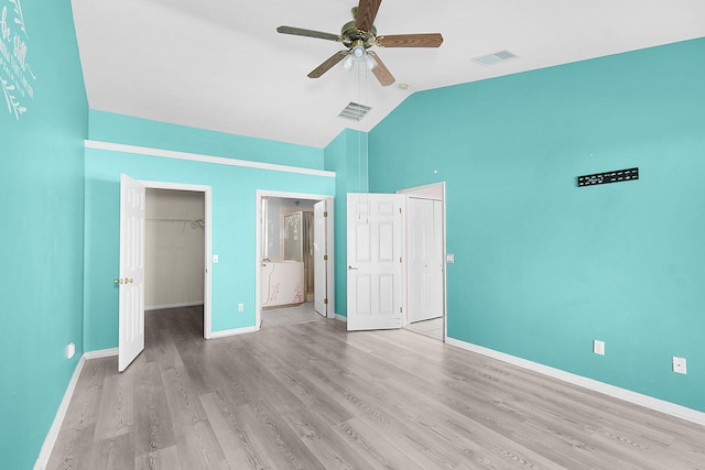 unfurnished bedroom featuring vaulted ceiling, a spacious closet, light hardwood / wood-style flooring, connected bathroom, and ceiling fan