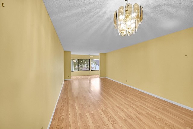 unfurnished room with baseboards, a textured ceiling, light wood-style flooring, and a notable chandelier