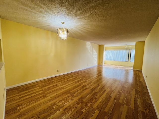 spare room with a textured ceiling, an inviting chandelier, and hardwood / wood-style flooring