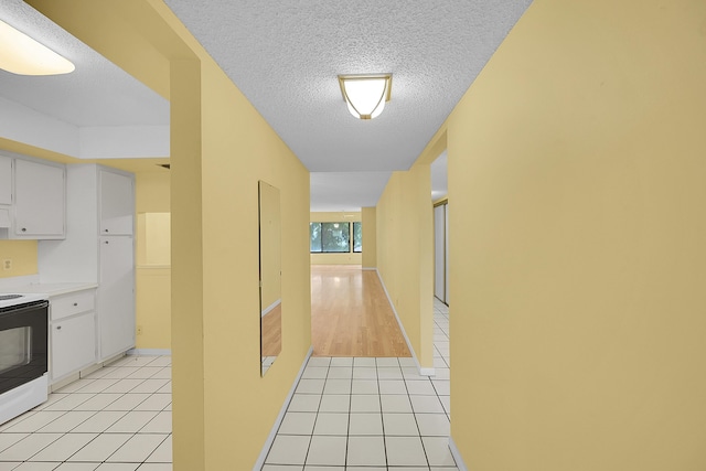 corridor featuring baseboards, a textured ceiling, and light tile patterned flooring