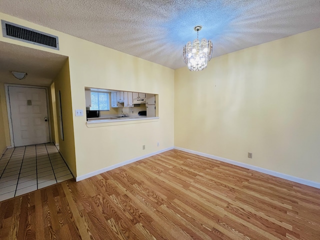 interior space with a textured ceiling, a chandelier, and light wood-type flooring