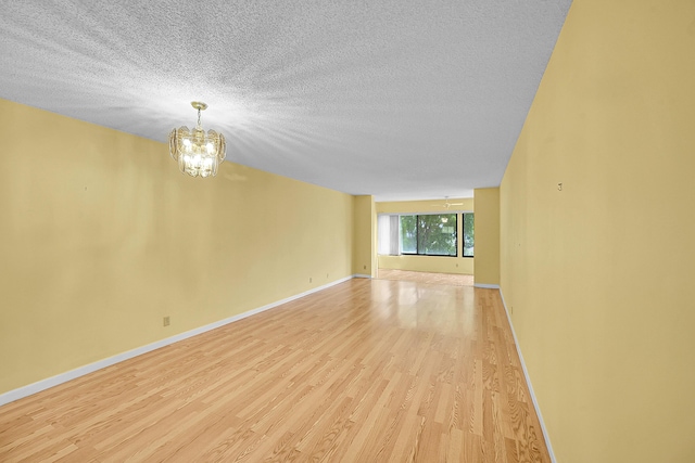 unfurnished room with a textured ceiling, a chandelier, baseboards, and light wood-type flooring