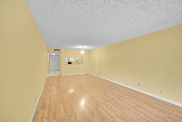 spare room with a textured ceiling, visible vents, baseboards, and light wood-type flooring