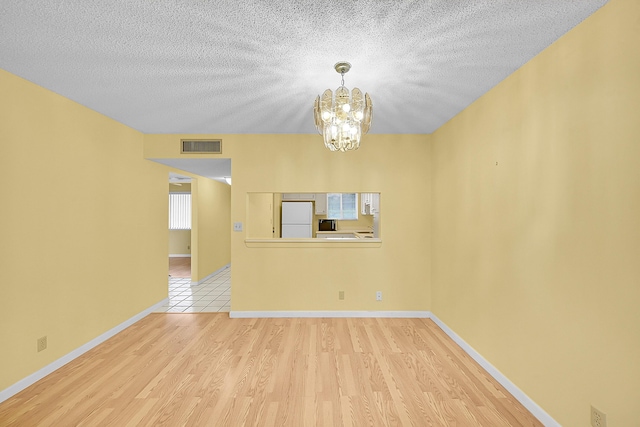 unfurnished living room with light wood finished floors, a textured ceiling, a chandelier, baseboards, and visible vents