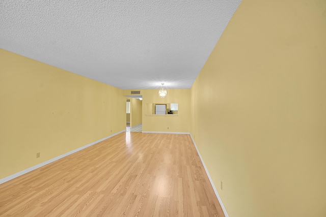 unfurnished living room featuring light wood-style floors, baseboards, and a textured ceiling