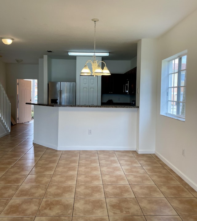 kitchen featuring light tile patterned floors, dark stone countertops, kitchen peninsula, and stainless steel fridge