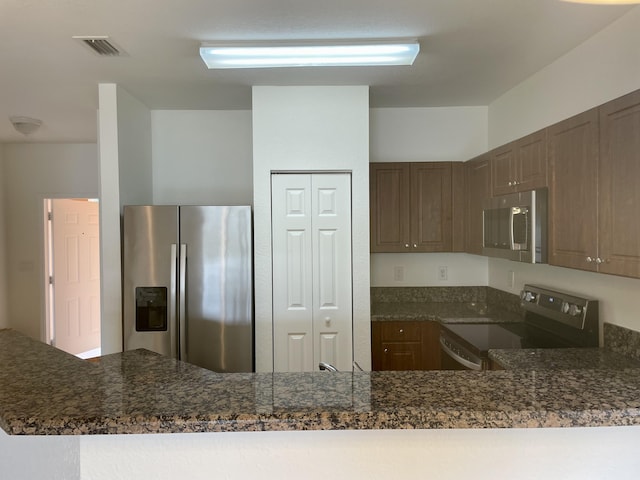 kitchen featuring stainless steel appliances, kitchen peninsula, and dark stone counters