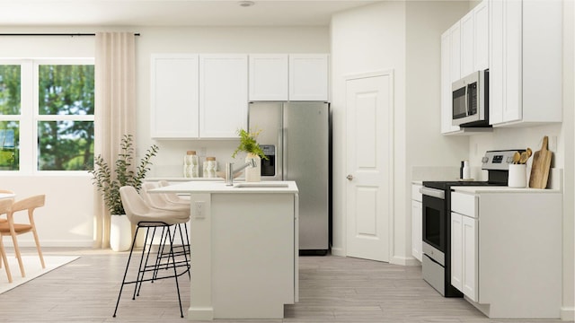 kitchen featuring stainless steel appliances, white cabinetry, a kitchen island with sink, and a breakfast bar area