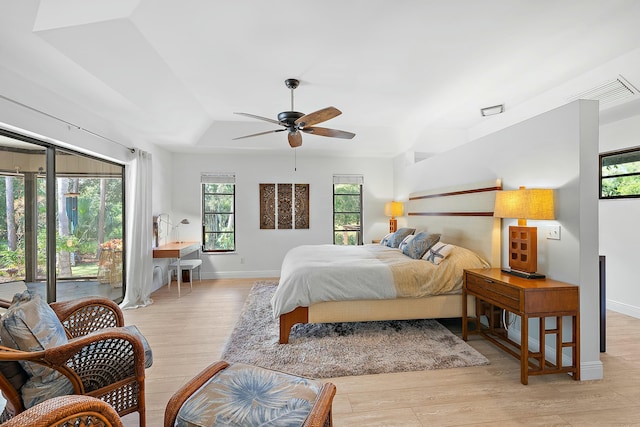 bedroom featuring ceiling fan, access to exterior, light wood-type flooring, and a tray ceiling