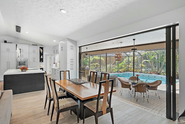 dining space featuring vaulted ceiling, a textured ceiling, and light wood-type flooring