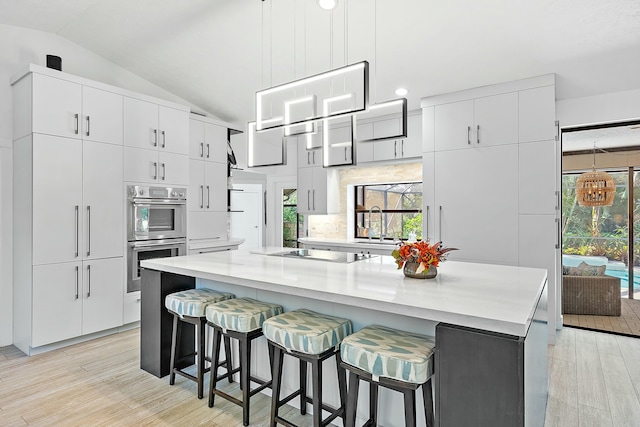 kitchen featuring a kitchen island, double oven, white cabinets, a kitchen bar, and black electric cooktop