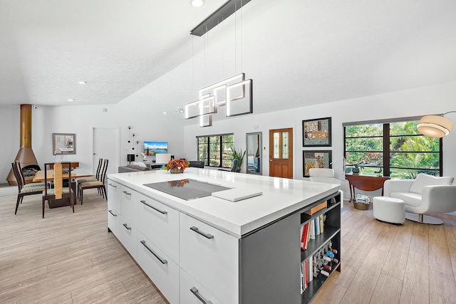 kitchen featuring black electric stovetop, white cabinets, a kitchen island, decorative light fixtures, and light wood-type flooring