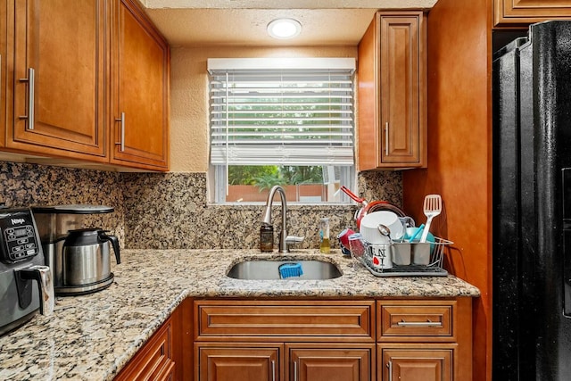 kitchen featuring black fridge, light stone counters, and sink