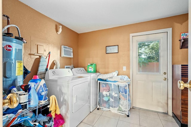 clothes washing area with a wall mounted AC, washing machine and clothes dryer, light tile patterned floors, and electric water heater