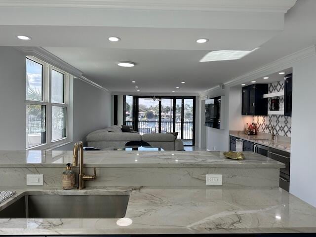 kitchen featuring dark cabinets, light stone countertops, crown molding, a sink, and recessed lighting