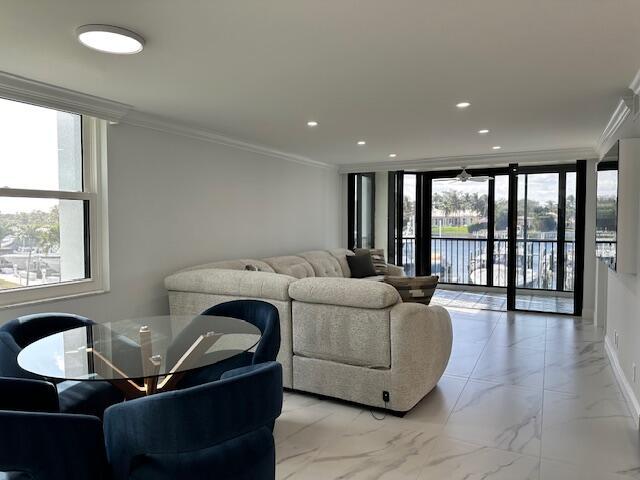 living area with ornamental molding, recessed lighting, marble finish floor, and a healthy amount of sunlight