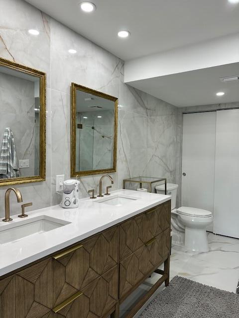 bathroom with marble finish floor, double vanity, a sink, and tile walls