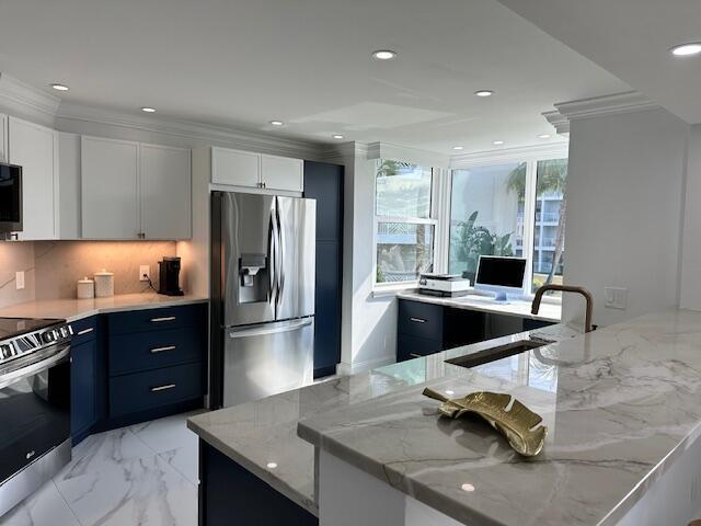 kitchen with light stone countertops, marble finish floor, stainless steel appliances, white cabinetry, and a sink