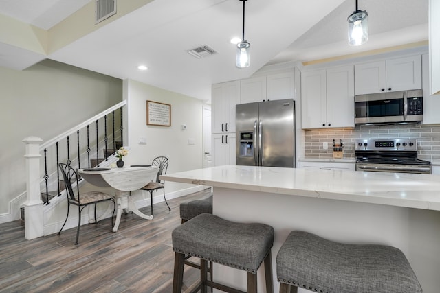 kitchen with light stone counters, decorative light fixtures, white cabinets, stainless steel appliances, and backsplash