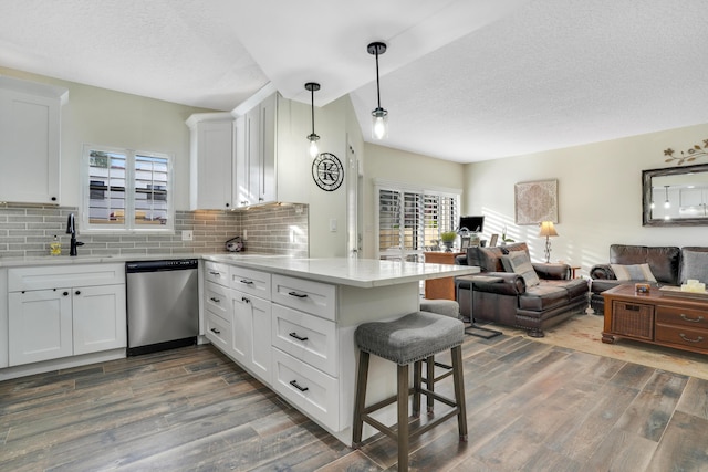 kitchen featuring pendant lighting, stainless steel dishwasher, kitchen peninsula, and white cabinets