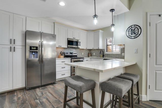 kitchen featuring white cabinets, a kitchen breakfast bar, backsplash, dark wood-type flooring, and appliances with stainless steel finishes