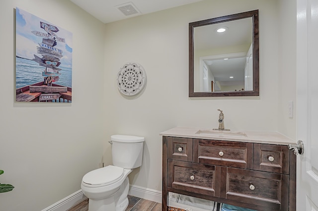 half bathroom featuring vanity, wood finished floors, visible vents, baseboards, and toilet