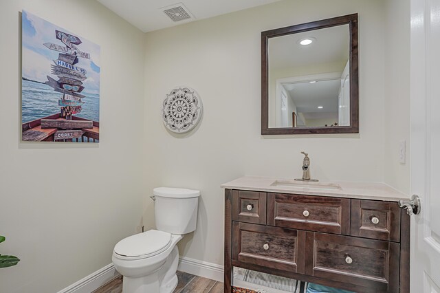 half bathroom with wood finished floors, vanity, baseboards, toilet, and visible vents