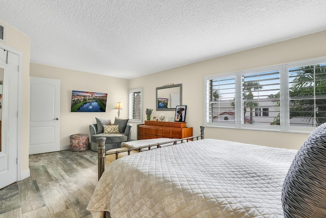 bedroom with wood finished floors, a textured ceiling, baseboards, and multiple windows
