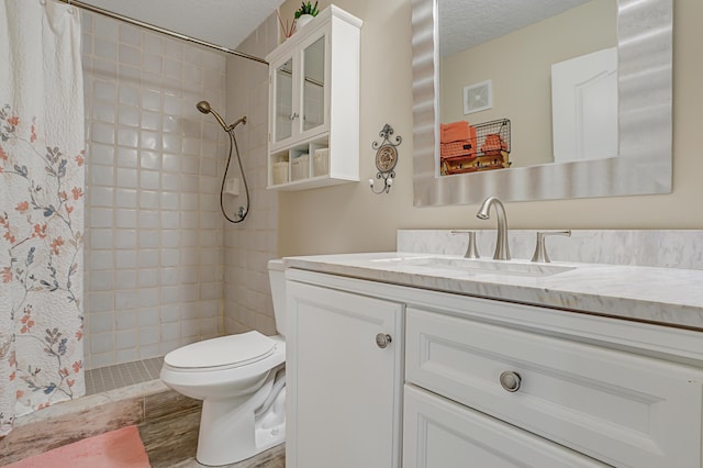 bathroom with a tile shower, toilet, vanity, and a textured ceiling
