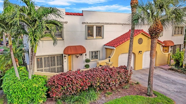 mediterranean / spanish-style home featuring an attached garage, a tiled roof, aphalt driveway, and stucco siding