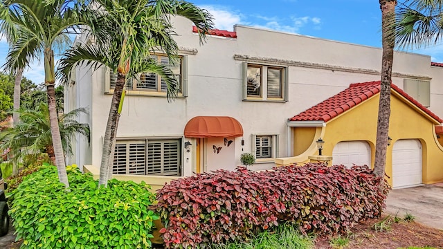 view of front of home with stucco siding, a tile roof, driveway, and a garage