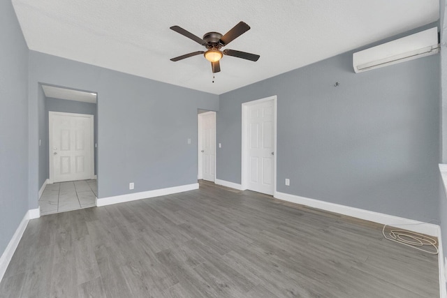 empty room with a textured ceiling, ceiling fan, a wall mounted air conditioner, and light hardwood / wood-style floors