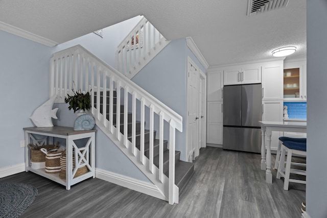 stairway featuring a textured ceiling, ornamental molding, and wood-type flooring