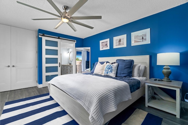 bedroom featuring dark wood-type flooring, a textured ceiling, ceiling fan, and a barn door