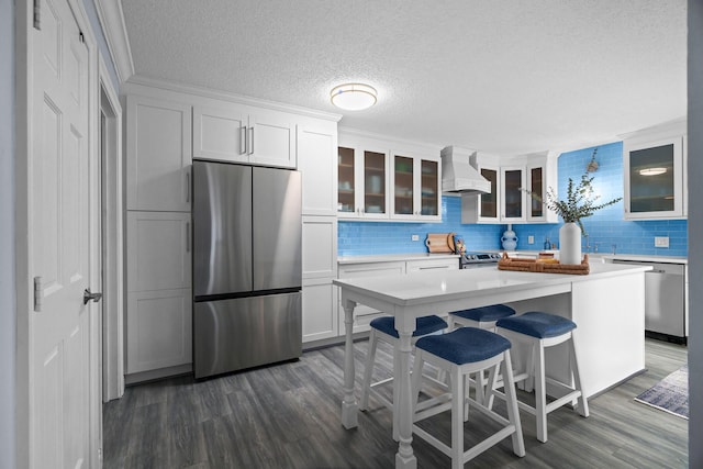 kitchen with appliances with stainless steel finishes, white cabinetry, a kitchen island, and custom range hood