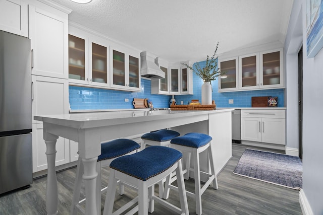 kitchen with a breakfast bar area, premium range hood, stainless steel fridge, white cabinetry, and backsplash