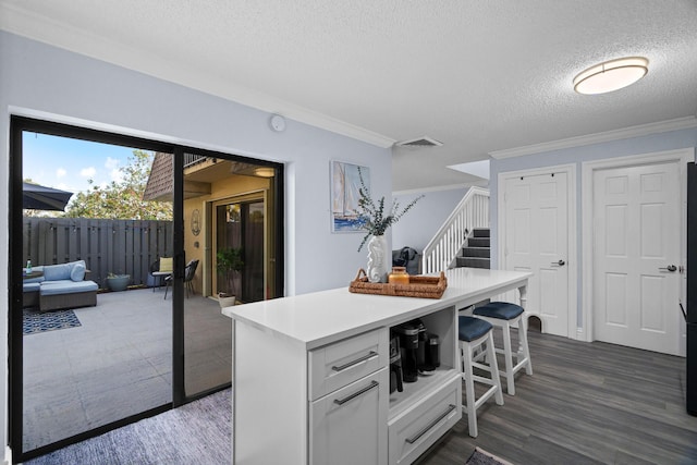 kitchen featuring a breakfast bar area, ornamental molding, a textured ceiling, a kitchen island, and white cabinets