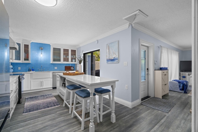 kitchen featuring dark hardwood / wood-style floors, decorative backsplash, white cabinetry, ornamental molding, and a kitchen breakfast bar