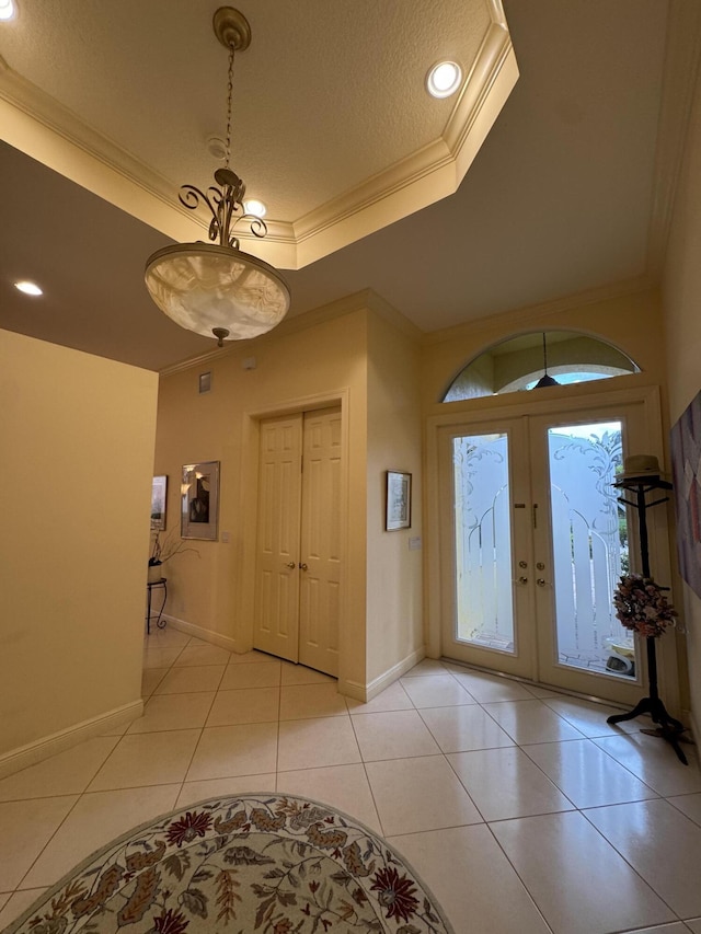 foyer with a raised ceiling, light tile patterned flooring, ornamental molding, a textured ceiling, and french doors